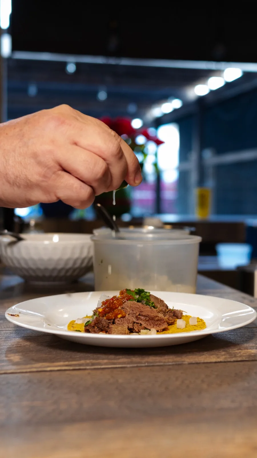 Una mano exprime limón sobre un taco recién servido en plato blanco.